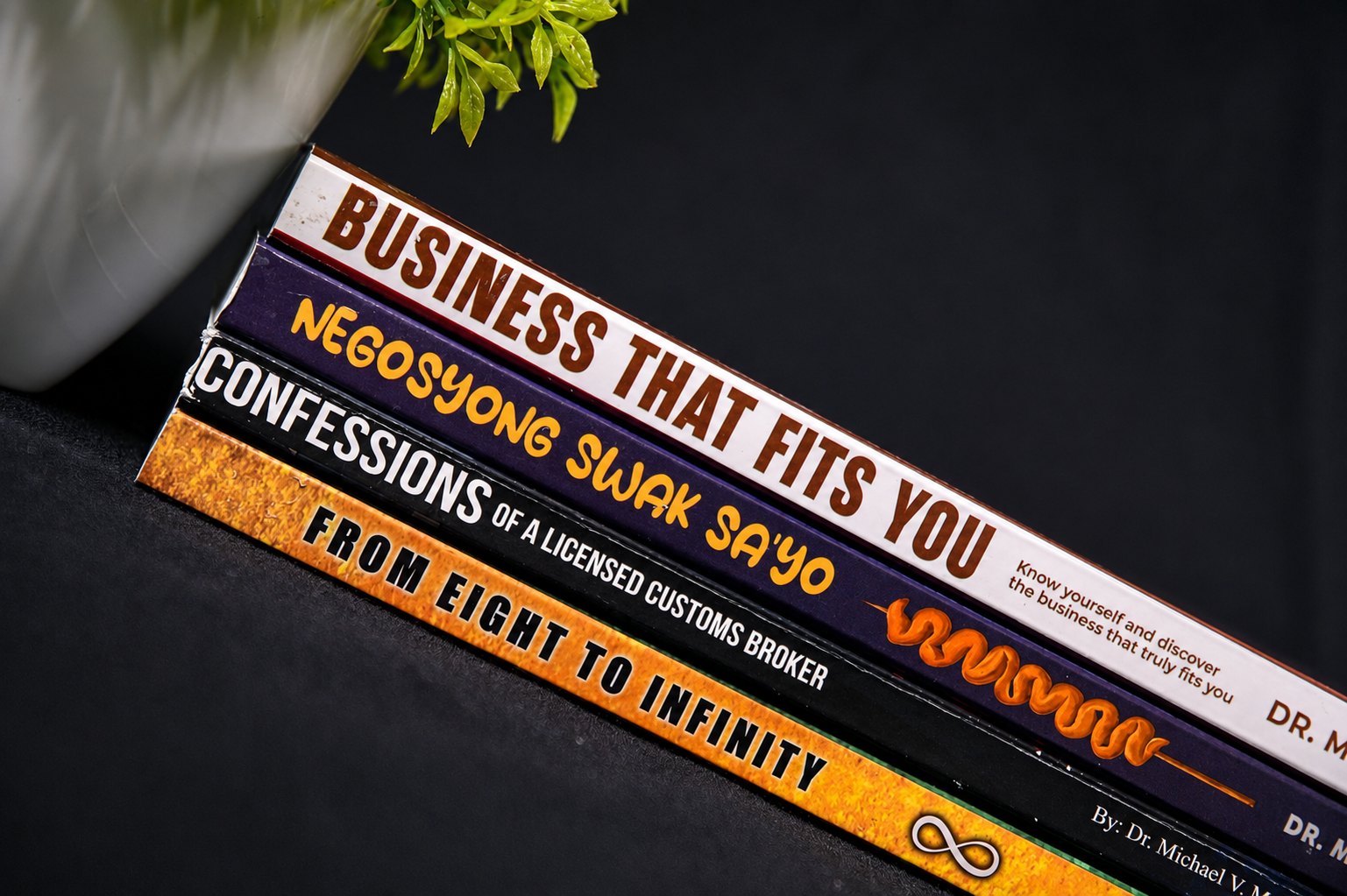 The four new books by Dr. Michael V. Maranan stacked together: Business That Fits You, Ang Negosyong Swak Sa'yo, Confessions of a Licensed Customs Broker, and From Eight to Infinity